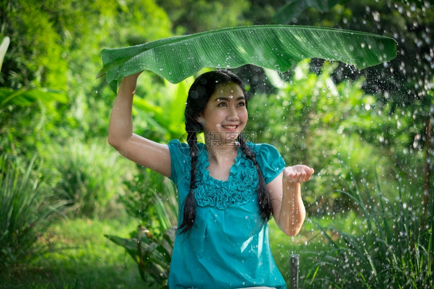 衬衫常设一种在绿花园背景下雨时一位年轻亚洲女身着香蕉叶的黑头发肖像图片