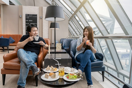 餐厅旅店亚洲夫妇在现代国际机场等待航班旅行和运输概念时坐并吃着小客店机场休息室的亚洲夫妇座席和吃饭班级背景图片