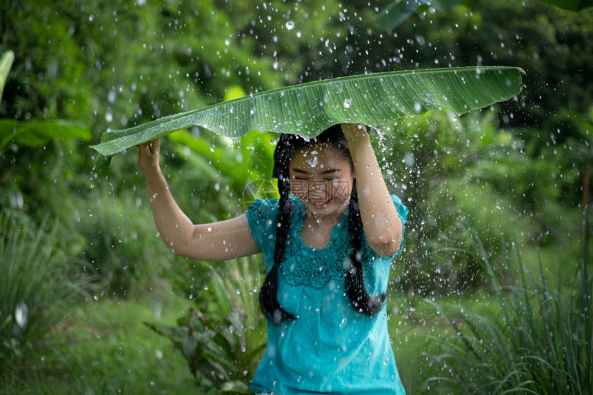 种植园场地分支在绿花园背景下雨时一位年轻亚洲女身着香蕉叶的黑头发肖像图片