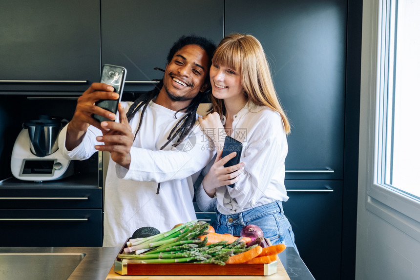 微笑男情怀非裔美籍男孩和白人女在厨房做自拍的图片
