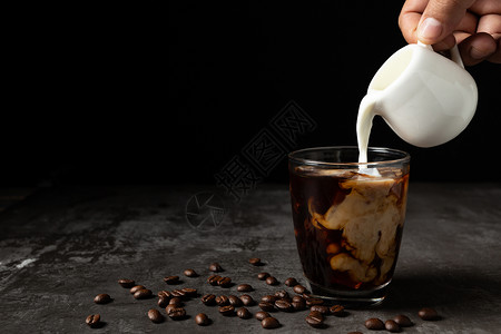 浇注木制的牛奶倒入桌上和黑底的冰咖啡品尝高清图片
