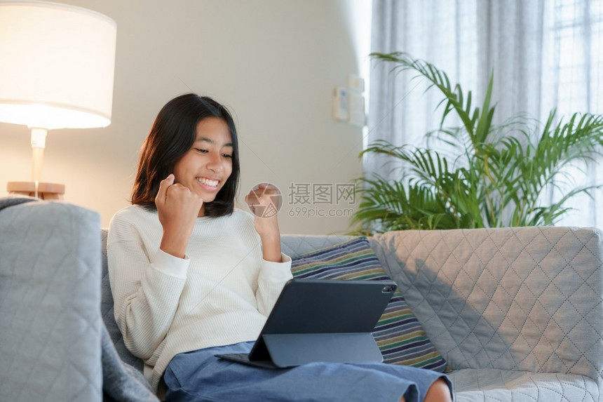 成功的亚洲快乐女孩在晚上坐客厅沙发时使用平板数字片但晚上却坐在客厅的沙发上放松女微笑图片