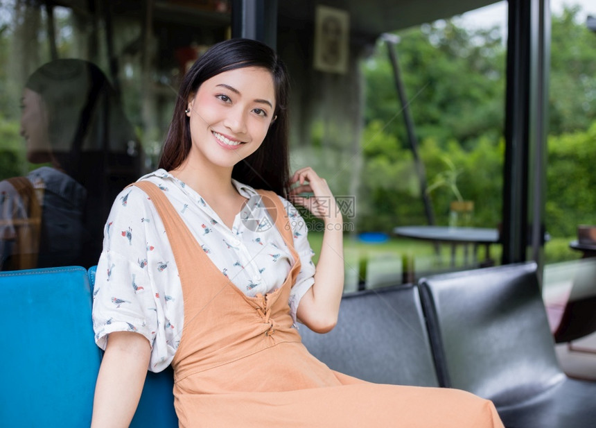积极的商业可爱亚洲女人坐在沙发或椅子上看着相机笑在放松时家里的肖像中快乐地微笑手图片