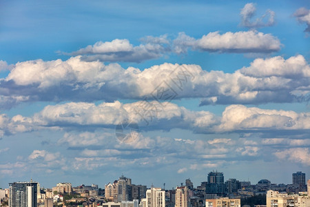 一种天际线城市风景蓝色的天空在城市上徘徊着白云并在太阳光下投阴影复制空间在城市上的蓝色天空中飘浮着大白云和灰城市景观背景图片