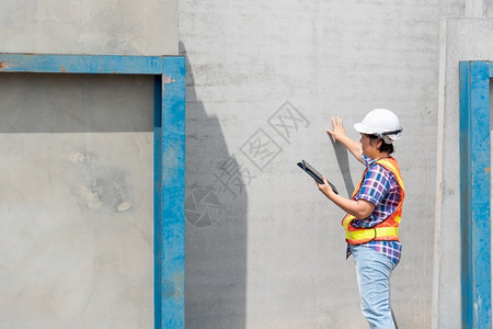 造星计划技术建筑学造亚洲女土木建筑工程或设计师身着头盔和安全背心工作并拥有一台触摸不定的平板电脑以查看建筑物或工地的蓝图或计划建筑工地的背景