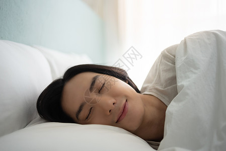 人们快乐的年轻睡得安稳早上在白床做梦假日是快乐笑的亚裔男在家眼闭着的时候躺在舒适软床铺枕头毯子和床垫上年轻的背景