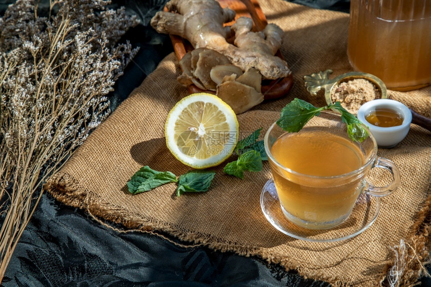 花朵热姜汁加柠檬和薄荷根小片姜汁含红糖和蜂蜜盛满棕色糖和麻布的蜂蜜热姜汁可以帮助身体变暖健康饮用新鲜的美食图片