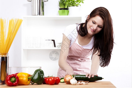 在一个厨房切黄瓜沙拉的小厨房里切黄瓜沙拉的年轻快乐女人红色的饮食图片