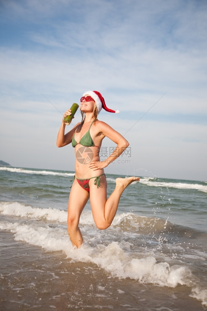 目的地季节圣诞戴帽子的快乐美女在海滩前边跳着舞图片