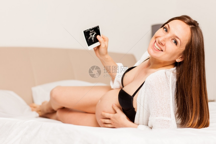 幸福孕妇躺在床上并拿着婴儿扫描图像的相片腹部奢华图片