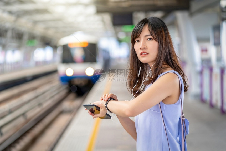 年轻的亚洲女乘客在大城市japanesechinese朝韩生活方式和日常通勤和运输概念上旅行时检查间并等待她在地铁列中朋友的等候图片