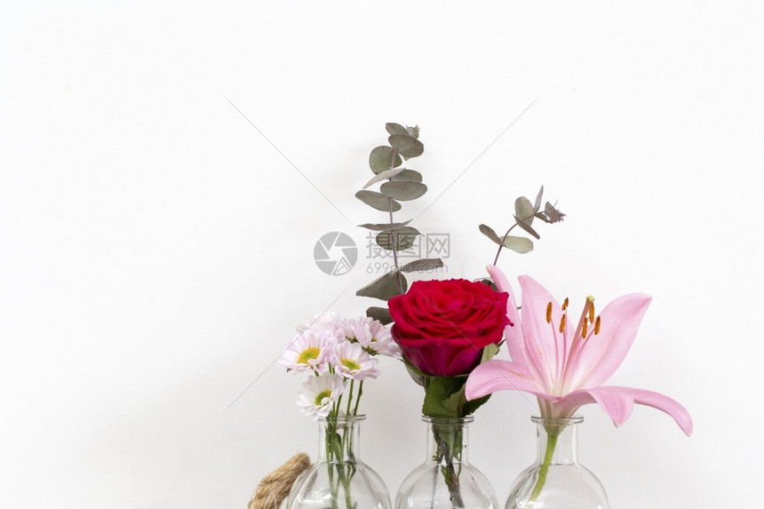小玻璃花瓶中有一系列红玫瑰、粉色百合和雏菊花图片