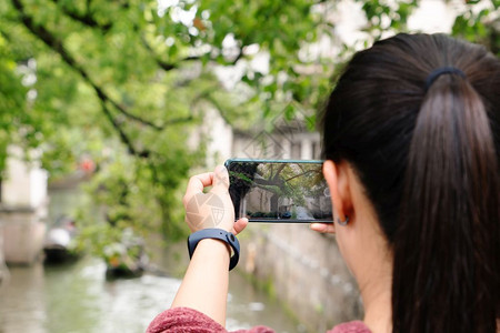 当地的模型城市在本地运河城市玩得开心的年轻女子使用智能手机摄影拍照片图片
