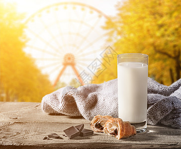 摩天轮秋在公园里一个雪轮的模糊背景牛奶和木桌上的羊角面包在木板上放着一个羊角面包纸一整块巧克力和件毛衣烘烤的面包店背景图片