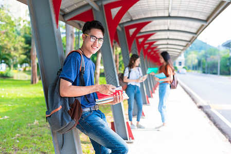 抱着书本的年轻亚洲学生站在步行道上图片