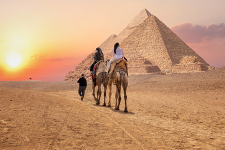 车夫座旅游埃及吉萨大金字塔附近骑骆驼的游客埃及吉萨大金字塔附近骑骆驼的游客假期沙丘背景