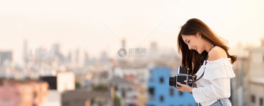 露齿的保持服用站在外边的漂亮亚洲女肖像却拿着带有建筑背景喜悦有乐趣无影踪全景的反光摄影机图片