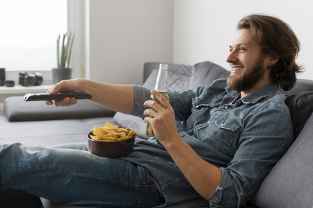 喝着酒拿着零食的男子在沙发上看电视图片