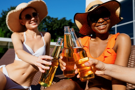 朋友在泳池附近喝着啤酒的瓶子快乐人在暑假玩得开心在泳池边户外的节日派对阳光浴朋友在泳池附近喝着啤酒的瓶子靠近微笑日光浴背景图片