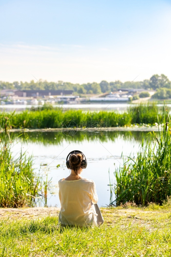 自然湖有耳机的女人听柔软音乐在冥想时候早上坐在河前就日出之后清晨坐在河前面着图片