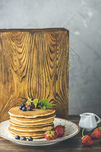 烤瓷冠美味的烤瓷炉小陶罐子上浅木制桌和灰色底的糖浆煎饼中含有白莓蓝和薄荷甜的目背景