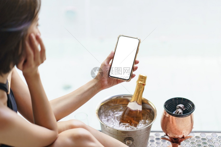 妇女手握空白屏幕移动电话在冰桶里装香槟瓶在泡沫池附近有两杯玻璃闪发光的寒冷派对图片