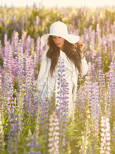 穿着白色帽子和外套夏日草原的时装年轻女子紫色的花绽放图片