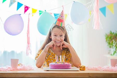 五彩纸屑帽子装饰风格快乐的小女孩在生日蛋糕上吹蜡烛与气球生日晚会一起充满花彩的背景和喜悦生日派对希望概念高加索女孩是梦幻般的微笑背景