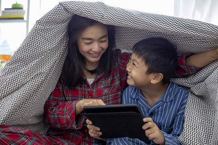 技术活的胶带一个快乐亚洲家庭母亲和儿子一起在客厅里玩游戏在数字平板电脑上玩游戏笑开心同时在家共度光接触高清图片素材