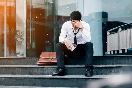 震惊失业或者下班后在行走道上坐着的疲劳或有压力商人受到压力的商人概念图片