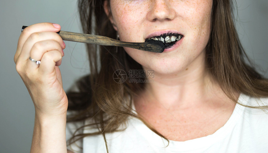 快乐的年轻女子用黑色牙膏和活炭刷白色背景上的黑牙刷用于齿美白干净的年轻女子用黑色牙膏和活炭刷白色背景上的黑牙刷用于齿美白色的竖起图片