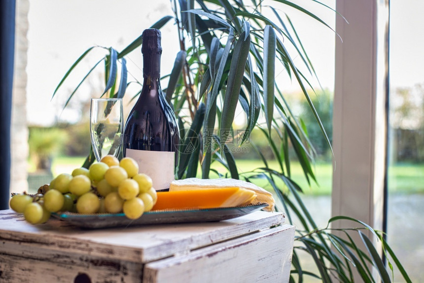 靠近窗户的桌子上放着葡萄和酒的奶酪拼盘配有舒适的椅子现代室内设计豪华装饰食物和室内概念美味的奶酪拼盘靠近窗户的桌子上放着葡萄和酒图片