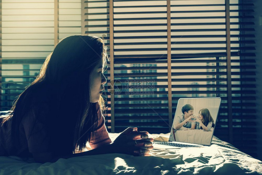 坐在床边看着幸福的亚洲爱人透过科技笔记本电脑在黑暗卧室的床上低光环境戏剧概念下坐卧着随意的男朋友失智图片
