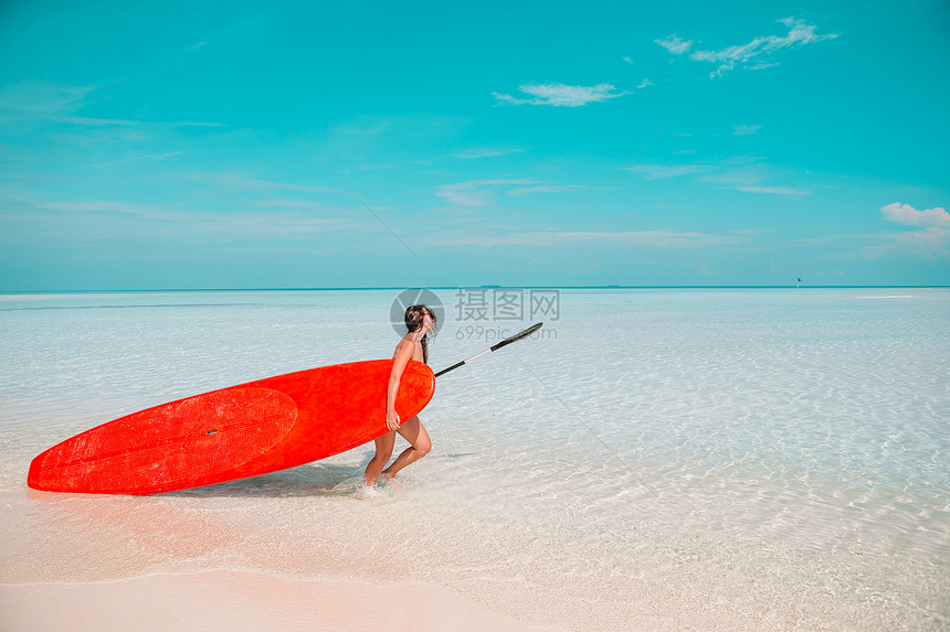 笑美丽的冲浪女子准备在异国情调的假期用红色桨板在绿松石海中冲浪旅行波图片