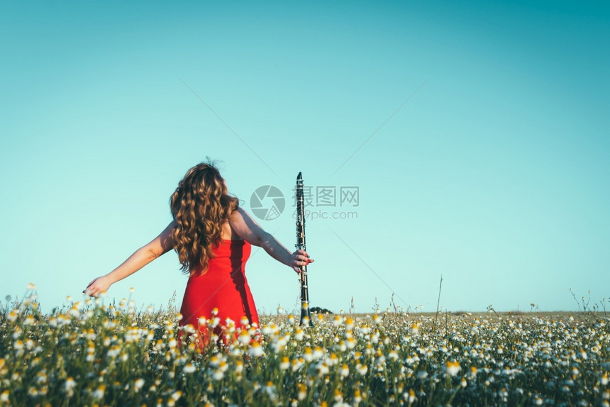 穿着红礼服和单簧管的女子在田里享受自由交响乐器红色的图片