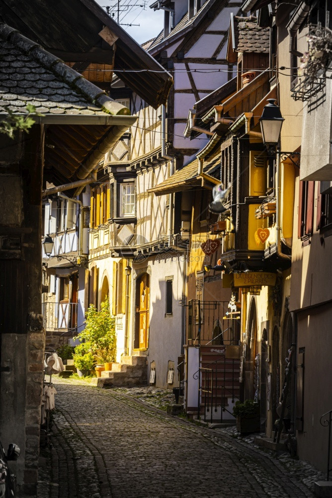 法国阿尔萨斯州Eguisheim中世纪镇一小条狭街道上带有可腐石的多彩色半形房屋葡萄酒摄影园图片