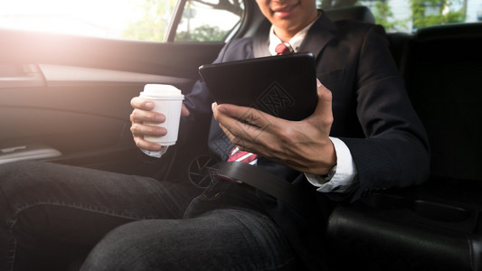 年轻的金融男人商在汽车中工作喝咖啡时使用平板电脑图片