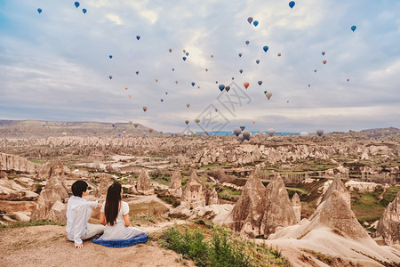 亚洲情侣看着多彩的热气球在土耳其卡帕多西亚山谷上飞过爱的浪漫时光地标爬坡道运输背景图片