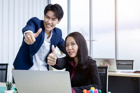 假小子专业的亚洲人行政员商业伙伴与男女商人露出拇指在笔记本电脑上工作并充满信心地有一个成功的商业计划在办公室一起微笑地着工作背景