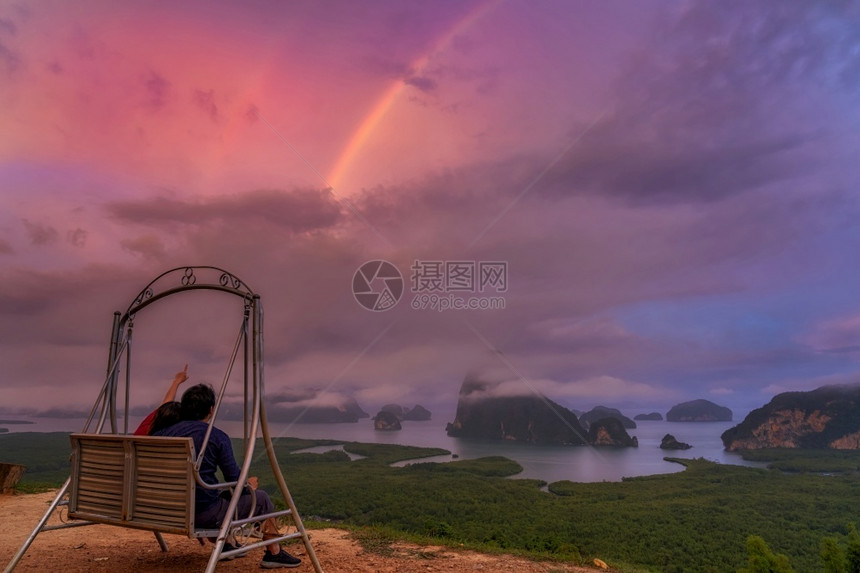 馕日落暮爱人的场景坐着并指向彩虹在日出时的同个南观景点奇幻上旅行与假日的概念图片