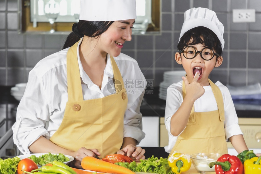 愉快新鲜的亚洲年轻母亲有儿子和的亚洲女青年母亲烹饪沙拉食品蔬菜配手持两番茄和胡萝卜为幸福家庭煮好食物的铃椒做饭厨房妈图片