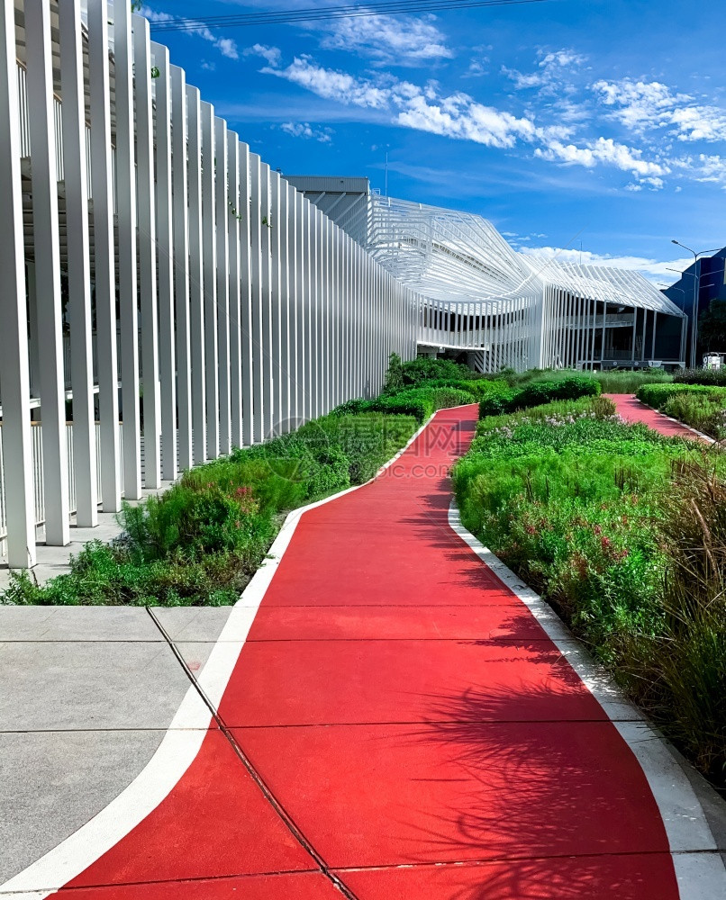 天空走道在购物商场附近的花园里跑空红色步行道在阳光明日配有绿色装饰植物的公园车轨上与阳光明日的绿色装饰植物一起运行在现代建筑旁进图片