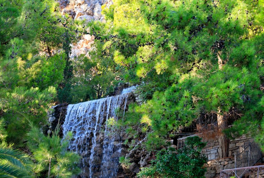 泡沫希腊卢特拉基公园Loutraki绿地中海松树和棕榈的阴影下在希腊卢特拉基山脚边的一座大瀑布上流出巨的石其中含有水位于希腊卢特图片