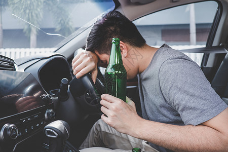 坐着安全年轻的亚洲人驾驶一辆醉酒的汽车一瓶啤酒然后在车轮面睡着了清醒图片