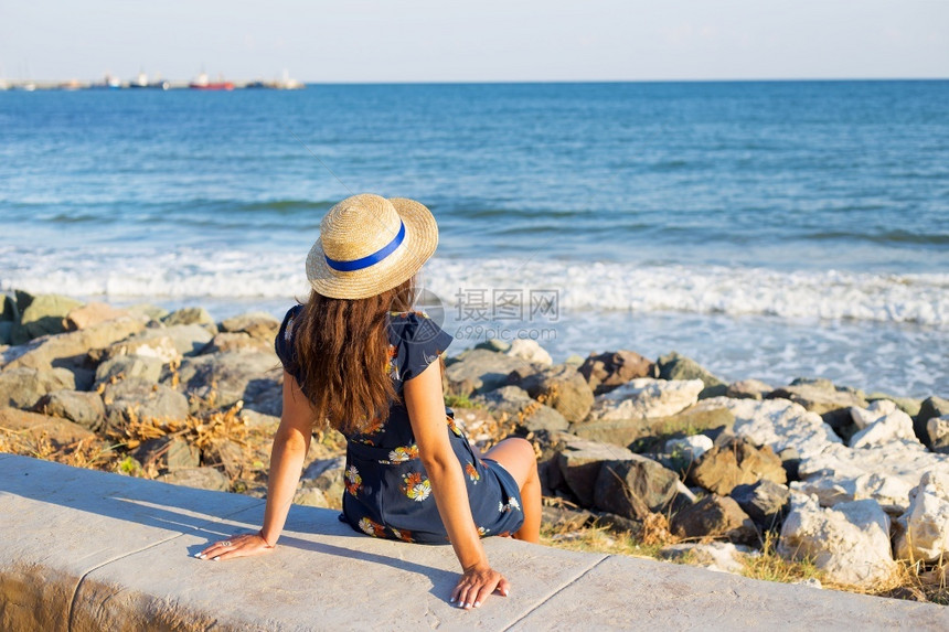 思考天空稻草戴着帽子的漂亮女孩坐在海边石块上戴着帽子的漂亮女孩坐在海边图片