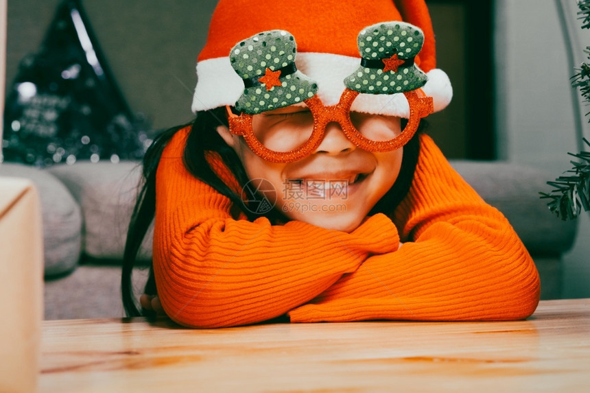 戴着圣诞帽的小女孩闭着眼睛坐在室内圣诞树附近许愿新年快乐圣诞周到房间帽子图片