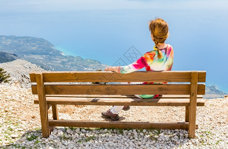 在希腊度假的中年妇女坐在山顶棕色木板凳上享受希腊假期背部最佳岛图片