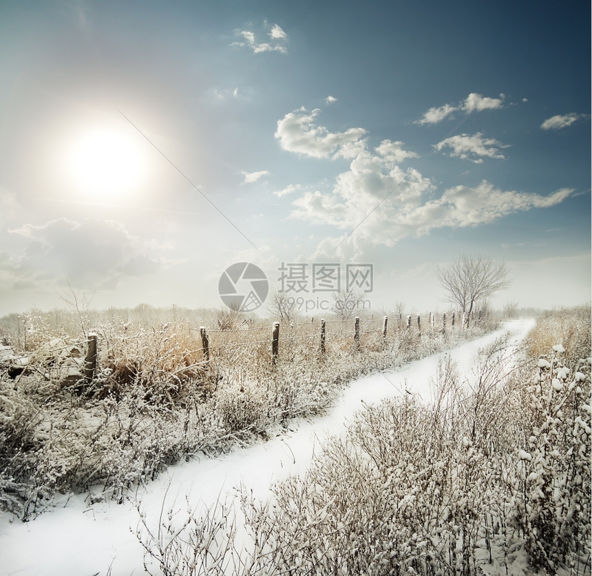 树云层下一片田地的雪覆盖道路经过围栏阳光宁静图片