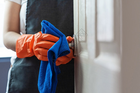 旋钮妇女手拿橙色橡胶套在门面触摸时打扫门把手用蓝色清洁布和对CoronaCOVID19预防概念的感染家政庭背景图片