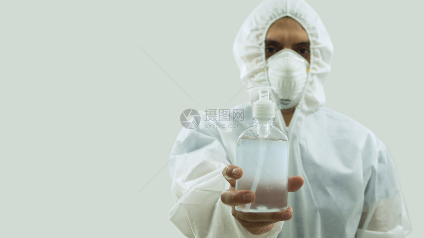 外科医生健康人们戴着面具和白色生物防护服的医在白色背景的前中手持一瓶凝胶酒精戴着面具和生物防护服的医在白色背景的前中手持一瓶凝胶图片